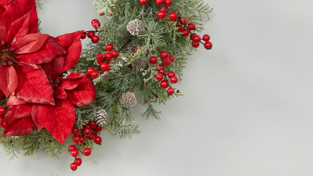 A snapshot of a Christmas wreath with red poinsettias and berries.